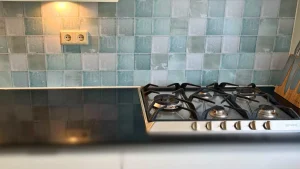 Opal antique tile backsplash in turquoise and sea green behind gas hob with socket cutout