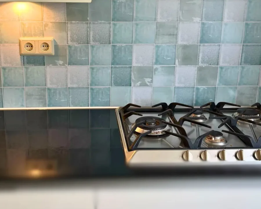 Opal antieke tegel spatwand in turquoise en zeegroen achter gasfornuis met stopcontact uitsparing