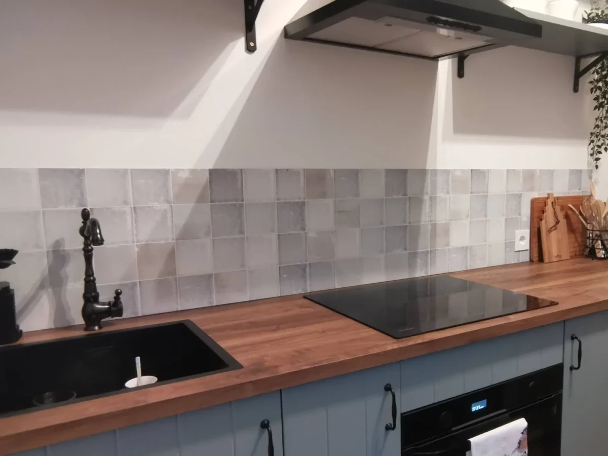 Ghost antique tile backsplash in grey and beige tones in kitchen with blue-green cabinets and wooden countertop