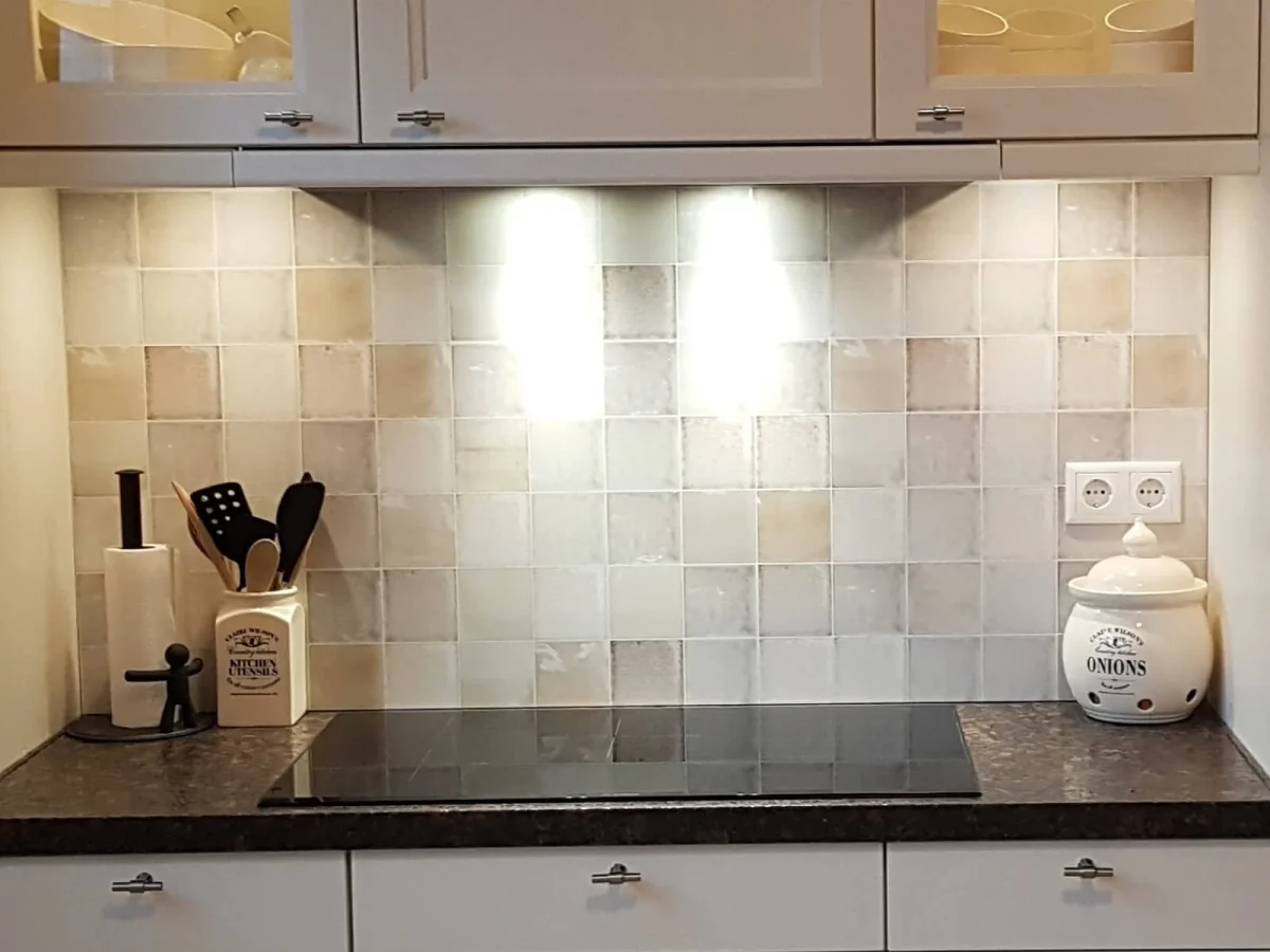 Crédence carrelage antique Swirl en tons crème et beige dans une cuisine avec armoires blanches et plan de travail en granit foncé