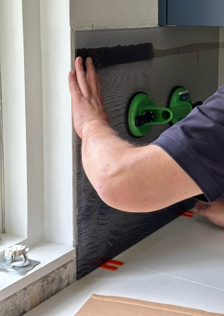 Kitchen backsplash being set against the wall with a suction lifter and pressed on by hand